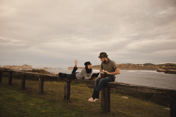 Man plying on drum near woman with notebook on bench on shore