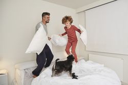Smiling man and boy playing with dog on bed