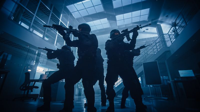 Masked Squad of Armed SWAT Police Officers Stand in Dark Seized Office Building with Desks and Computers.