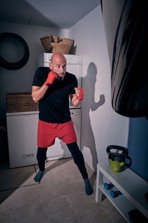 Man training boxing in the laundry room at home with a bag