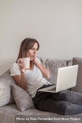Surprised woman on sofa with a cup of coffee working on her laptop in the morning 0K9yz4