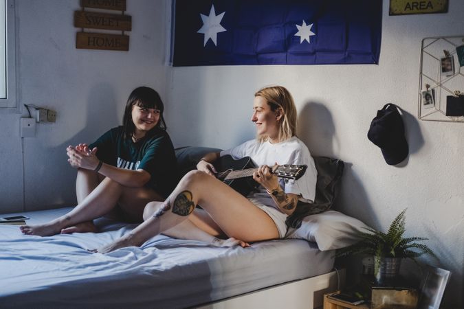 Lesbian couple playing guitar on bed