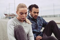 Young woman looking down at her shoes while resting after workout, boyfriend beside her
