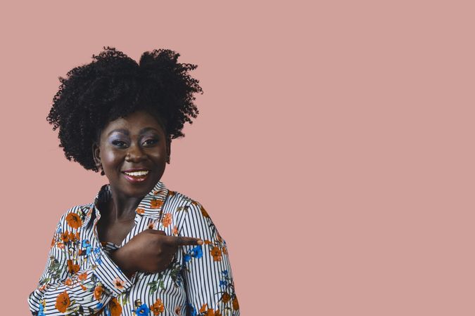 Studio shot of Black woman in floral print shirt pointing at something to the side