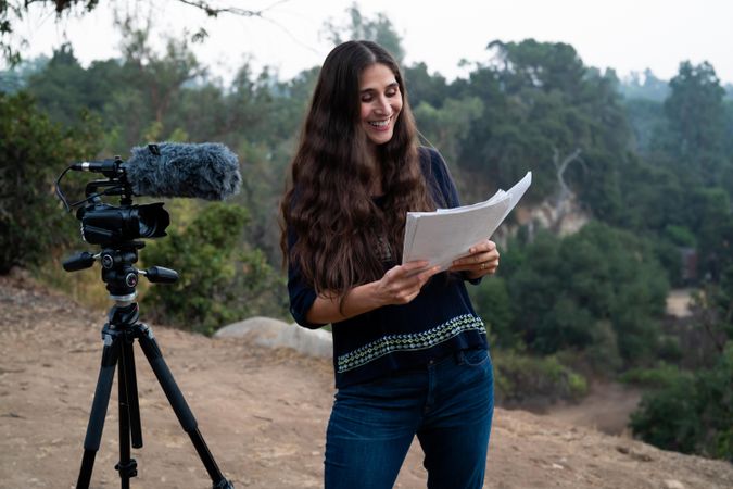 Woman standing next to camera and smiling while reading the script