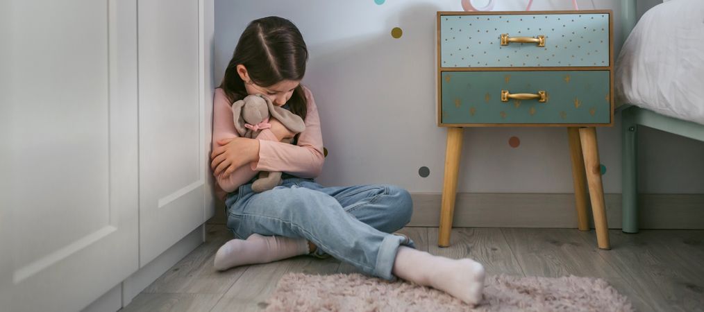 Sad girl hugging stuffed toy sitting on the floor