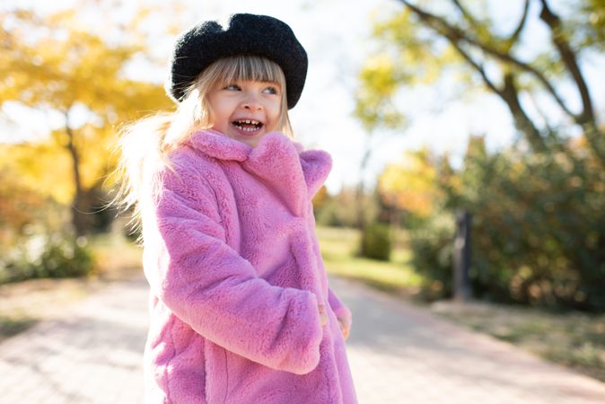 Smiling girl in pink coat standing in park