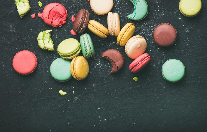 Assortment of multi-colored macaron pastries against a dark background, with copy space