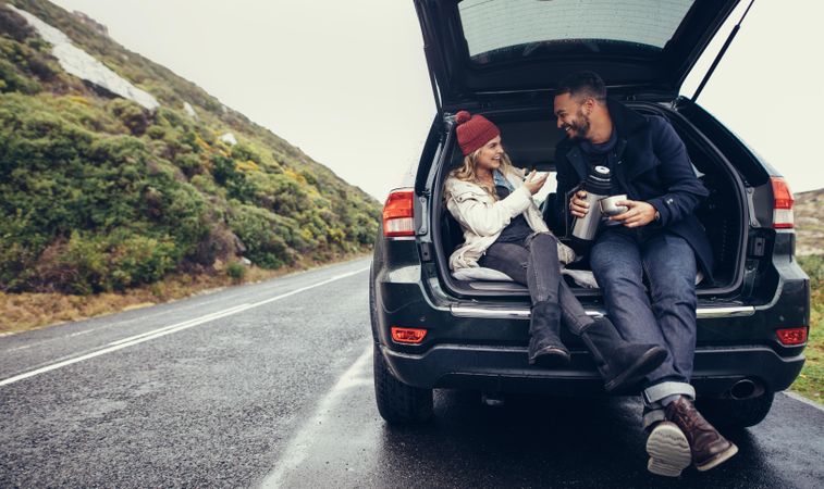 Man and woman sitting in car trunk and having coffee