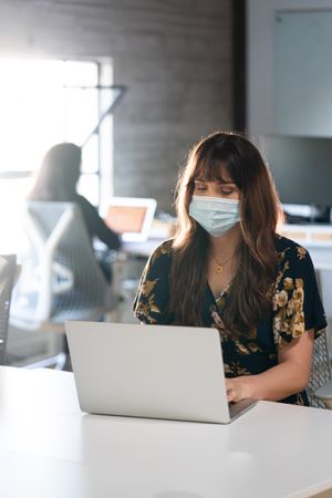 Transgender woman engineer writing code wearing medical mask