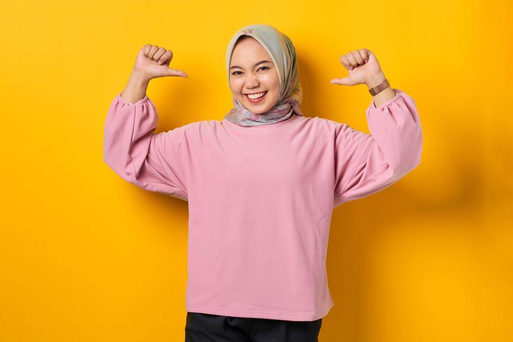Serious Muslim woman in scarf pointing both her thumbs to herself