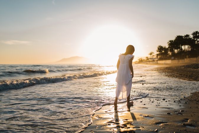 Adorable girl walking on seaside at sunset
