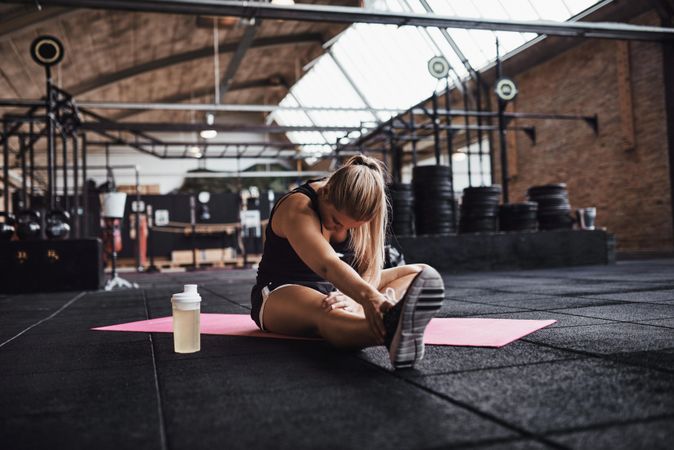 Woman stretching legs on mat in weightlifting gym