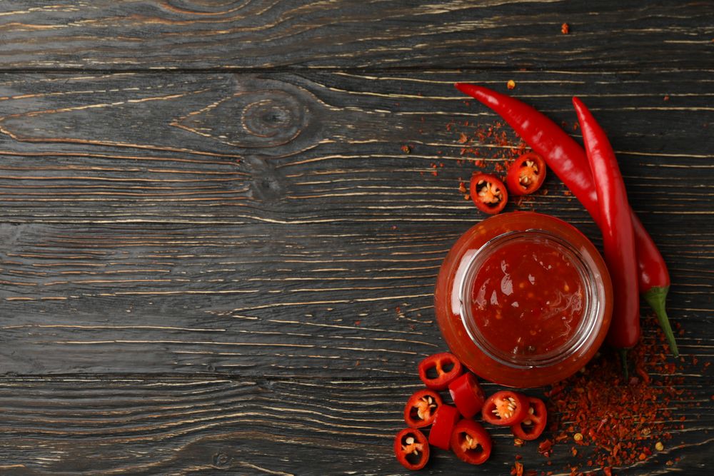 Chilli pepper and glass jar of sauce on wooden  background, top view