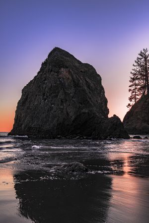 Large rock in the Pacific Ocean at dusk with beautiful purple orange sky, vertical composition