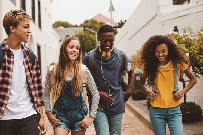 Smiling teenage friends wearing backpacks walking outdoors and talking