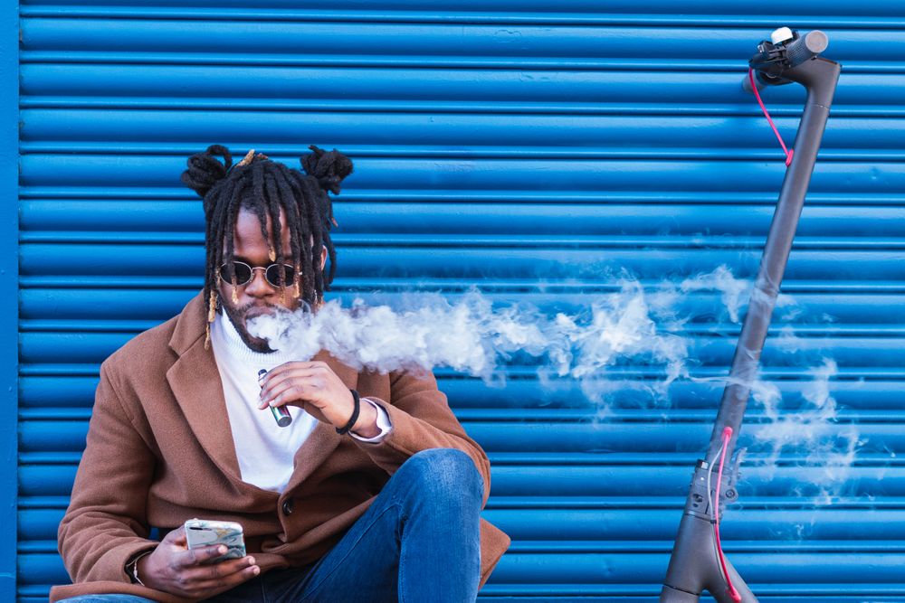 Hipster Black man with electronic cigarette using smartphone