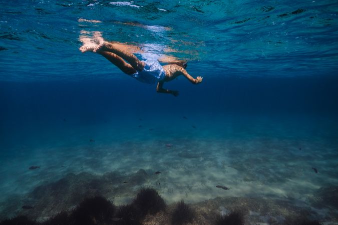 Unrecognizable kid snorkeling in blue sea