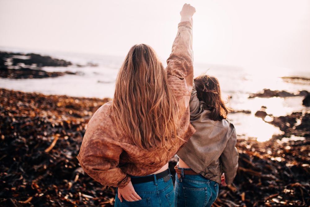 Two young women on the beach with one arm raised in victory