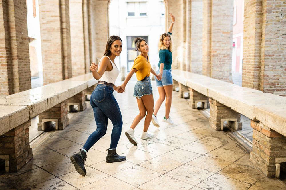Diverse female friends walking holding hands and looking around smiling