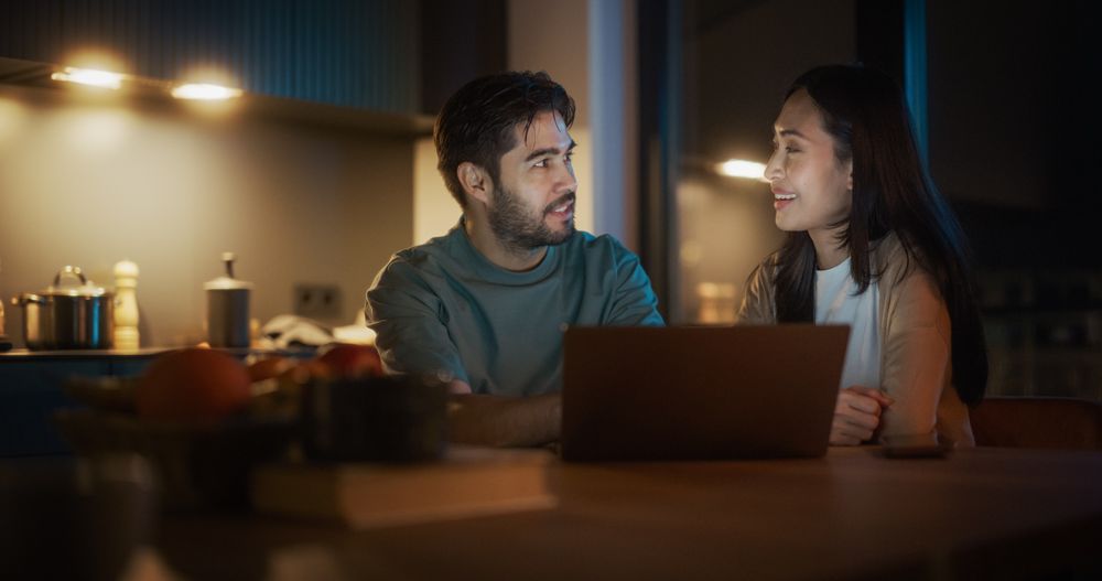 Portrait of Young Couple Using Laptop Computer While Sitting in the Kitchen at Home And Talking.