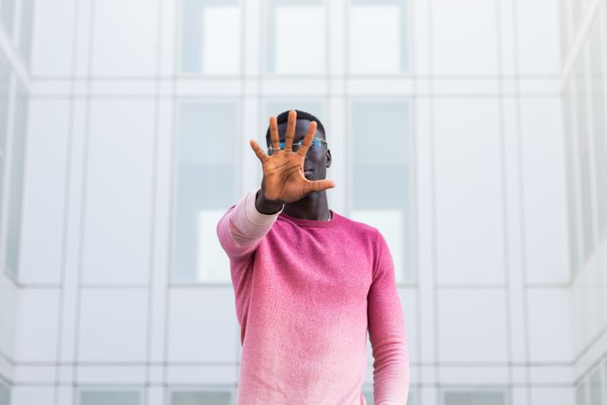 Black man covering face and showing stop gesture in city street