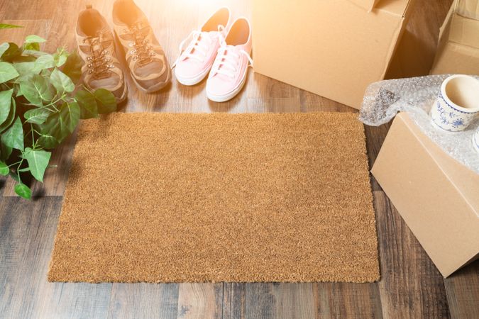 Home Sweet Home Welcome Mat, Moving Boxes, Women and Male Shoes and Plant on Hard Wood Floors