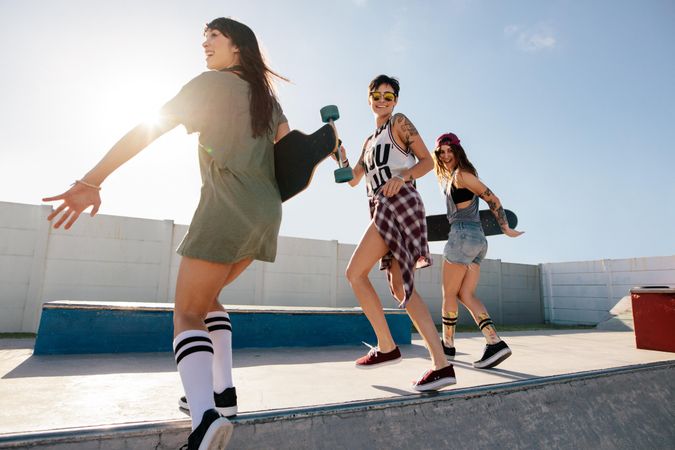 Three female friends running and jumping over skate park ramp