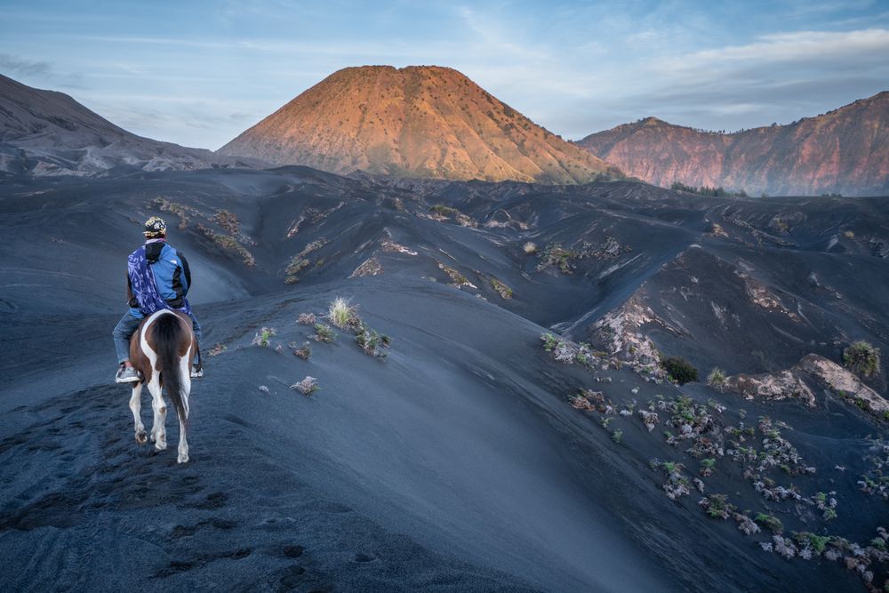 Backside of a man riding a horse in the mountains