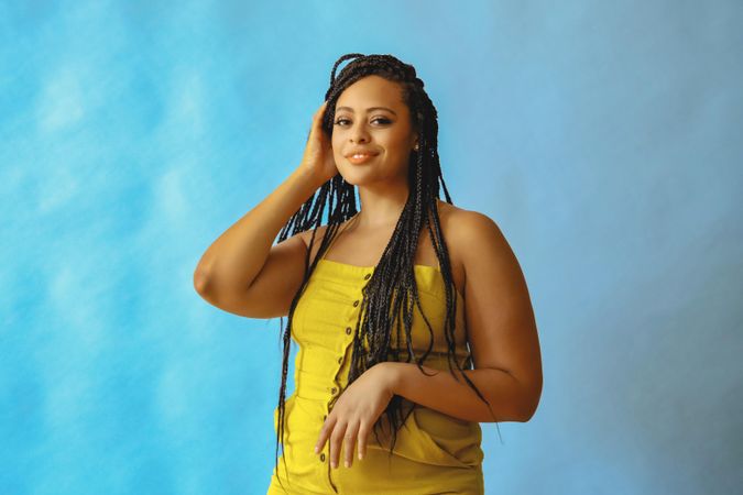 Relaxed female with long braided hair and hand to her head in yellow one piece
