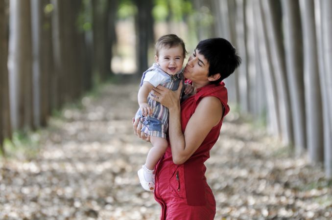 Woman kissing smiling little girl in forest