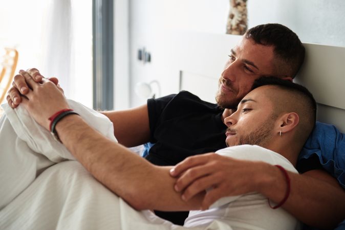 Smiling gay couple hugging on bed