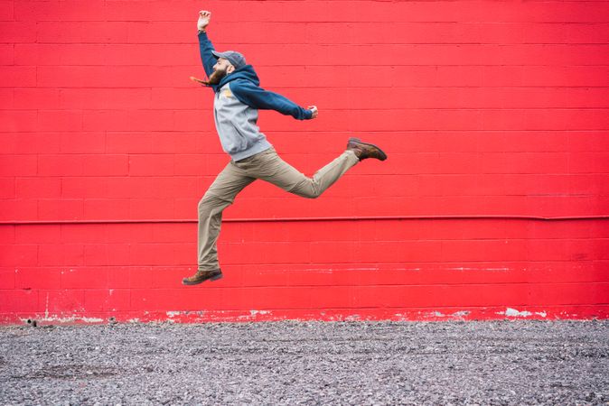 Bearded guy jumping near red wall