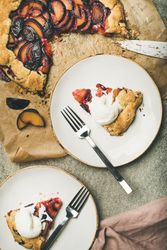 Two plates of fruit tart with whipped cream, forks, knife, on parchment paper, concrete background