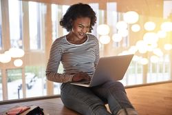 Woman sitting on floor smiling while working on her laptop