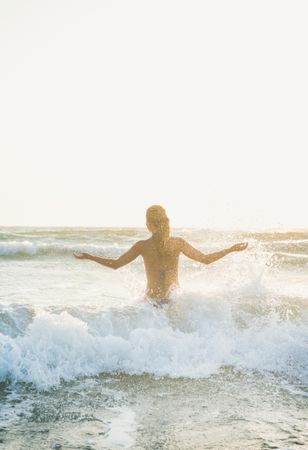 Rear shot of woman in waves at the beach with outstretched arms