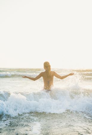 Rear shot of woman in waves at the beach with outstretched arms