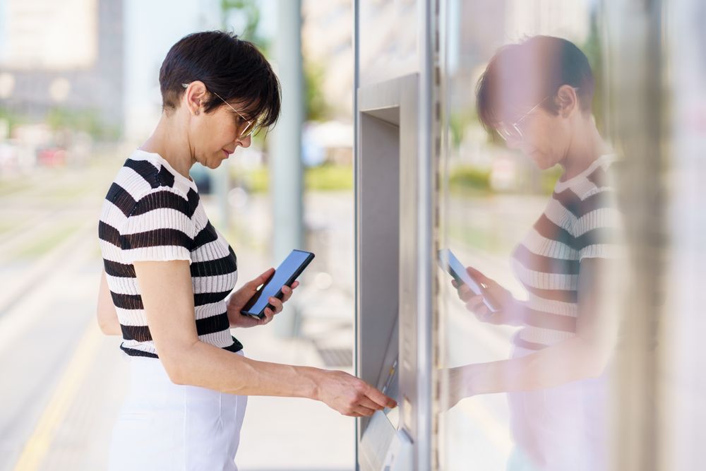 Woman holding phone while taking out money on ATM