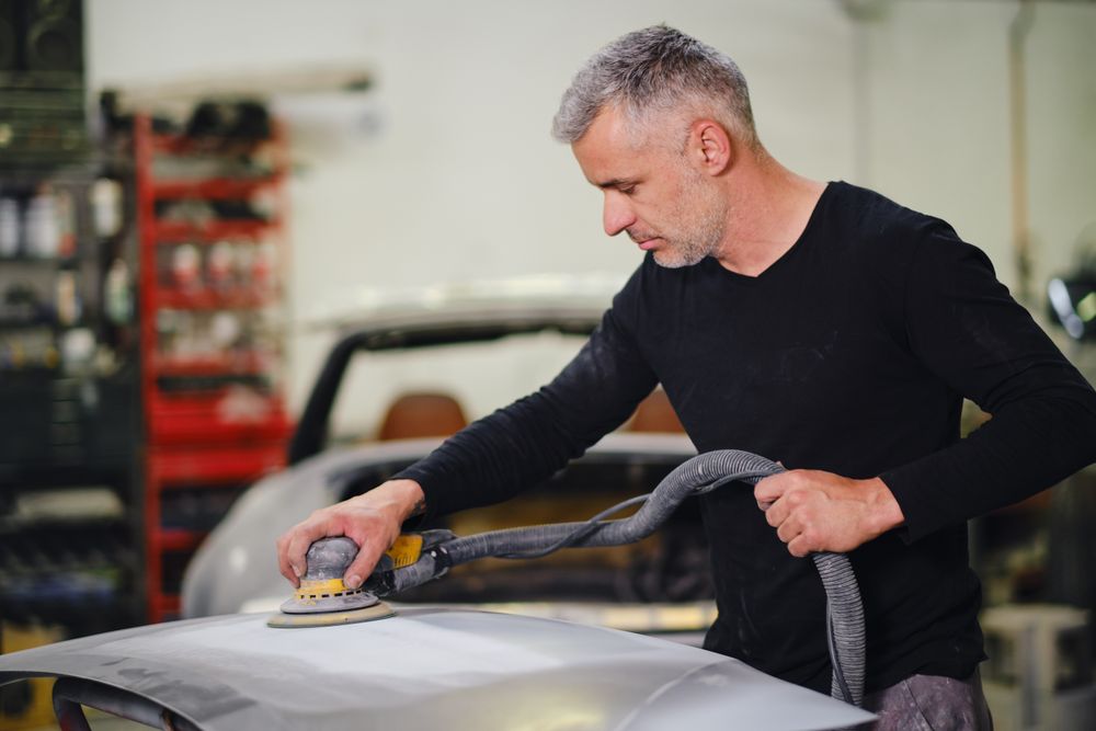Mechanic grinding paint from car detail