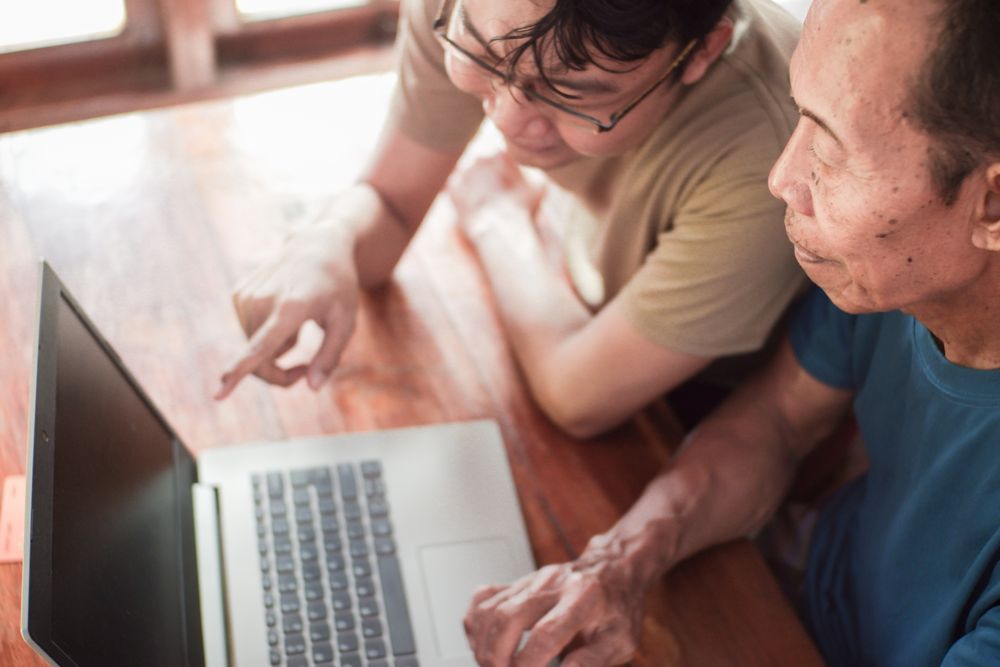 Happy adult son teaching older father using laptop