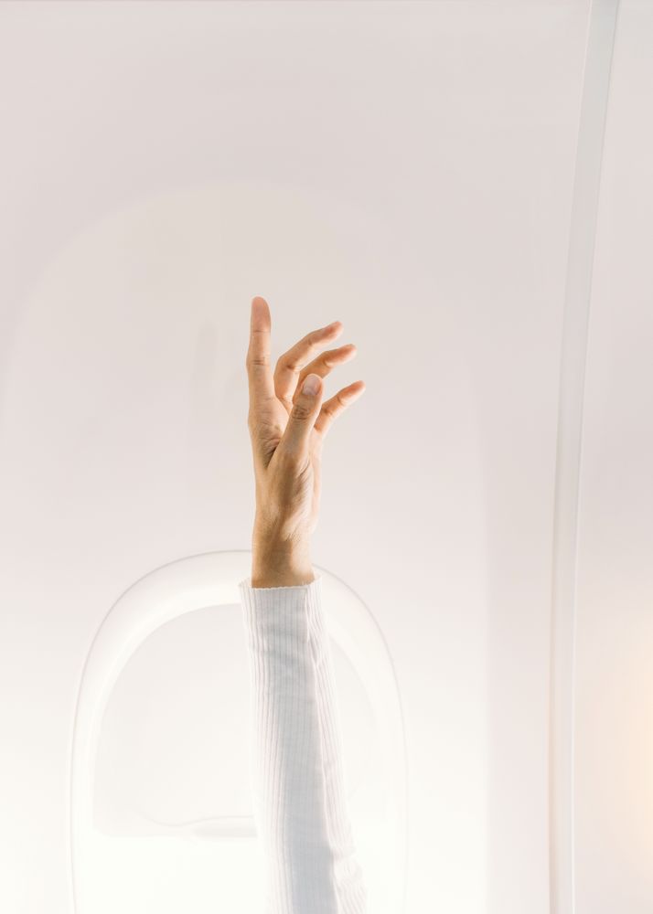 Person in white sweater raising hand up in plane