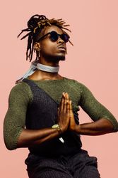 Young Black man with dreadlocks hair in meditation pose, wearing sunglasses and green shirt, relax with eyes closed doing gesture with hands.