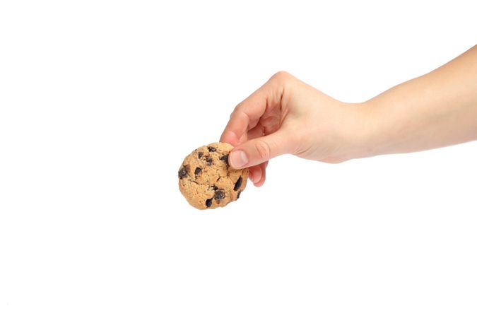 Woman holding tasty chocolate chip cookie on plain background, closeup