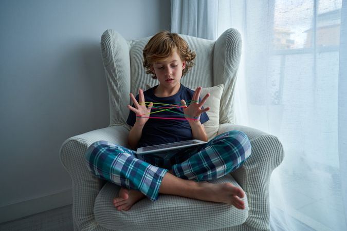 Concentrated boy playing cats cradle game in room