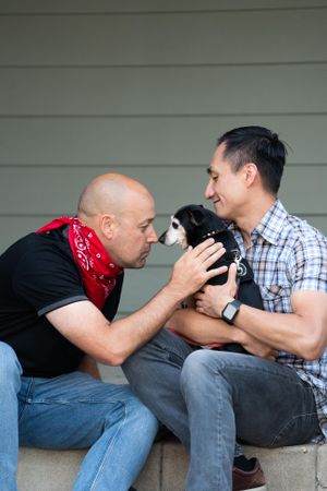 A man and his dog with their noses touching while sitting outside in front of their home