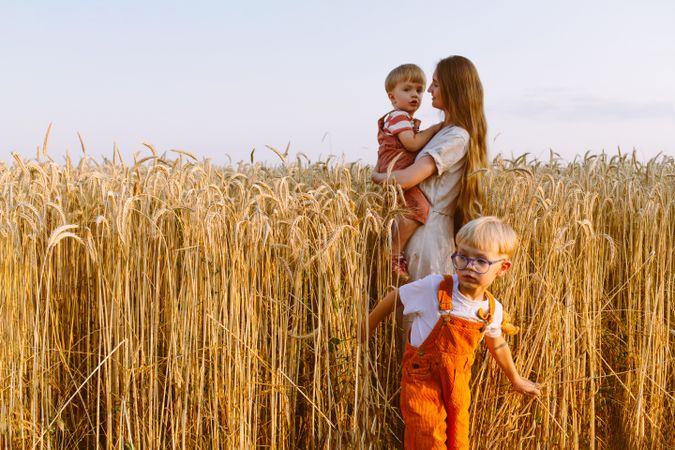 Young mother with little sons standing on wheat field in countryside
