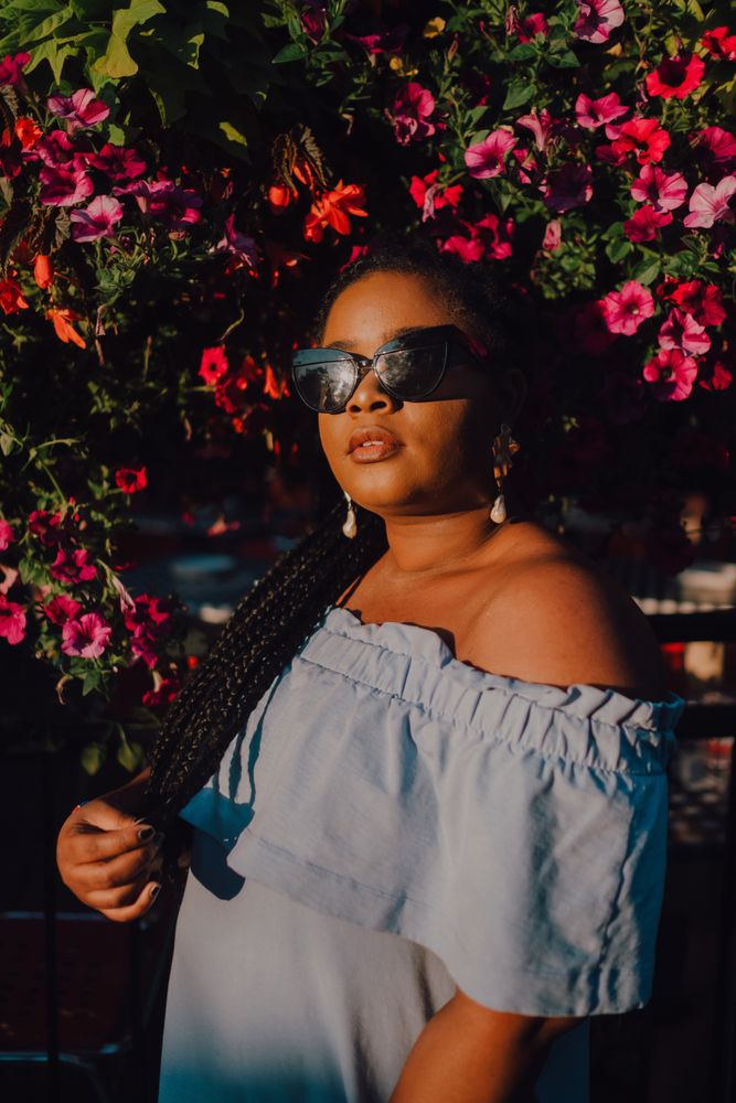 Joyful trendy Black woman in sunglasses standing beside blossomed tree