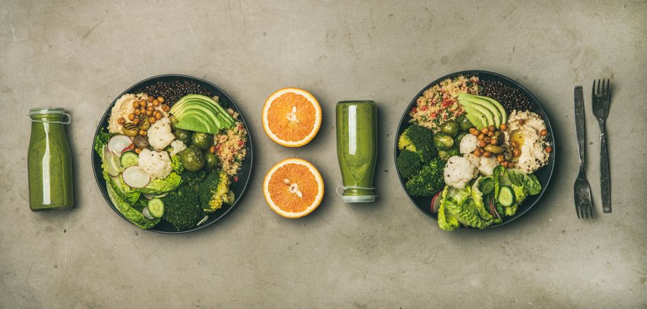 Two vegetarian bowls, with smoothie, orange halves, silverware, wide composition