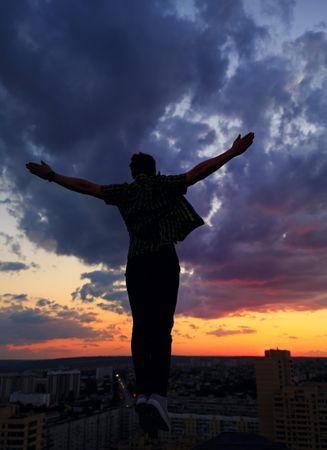 Out line of male with outstretched arms against a colorful dusk side