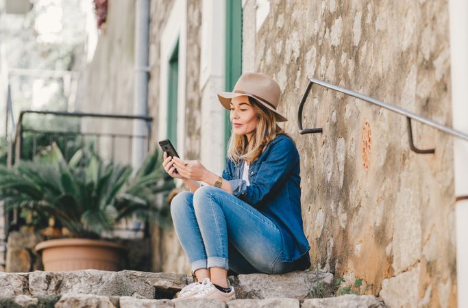 Woman with smartphone sitting on stone steps of stairs